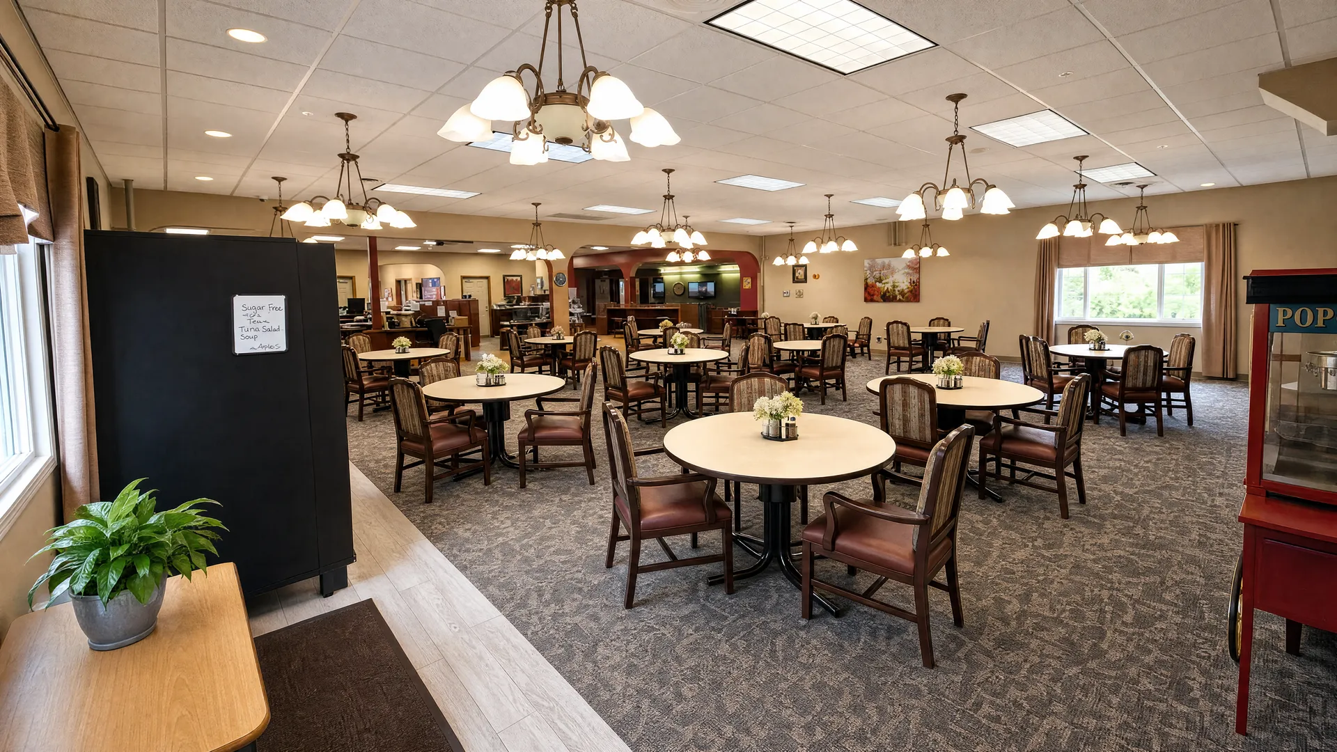 Main dining room with round tables beneath chandeliers at Nora Springs Care Center
